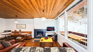 Una sala de estar moderna con chimenea, techo de madera y ventanas amplias que dan a un paisaje nevado.