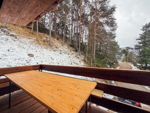 Een houten terras met een tafel en banken, met uitzicht op een besneeuwde heuvel met bomen.