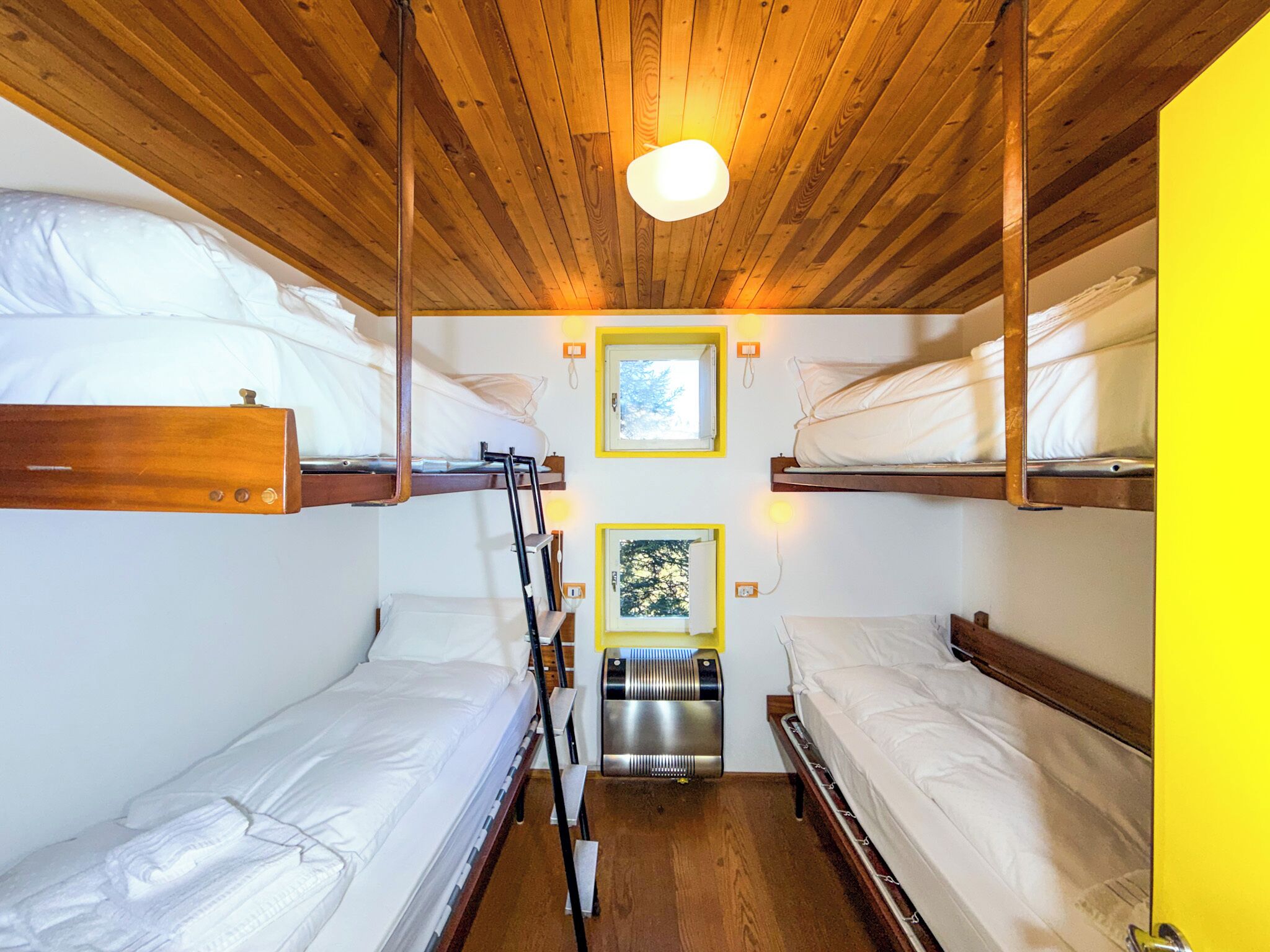 A compact room with bunk beds, wooden ceiling, and a small window with a view.