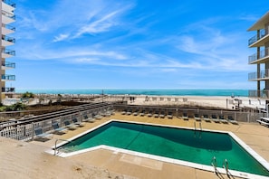 A swimming pool with a view of the beach and ocean, surrounded by lounge chairs and a fence. - Ocean-view condo with pool access, outdoor seating, central AC & WiFi (Gulf Shores)
