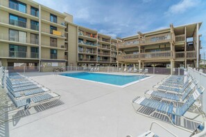 A multi-story hotel with a central swimming pool surrounded by sun loungers. - Ocean-view condo with pool access, outdoor seating, central AC & WiFi (Gulf Shores)