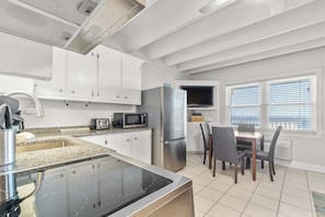 A modern kitchen with white cabinets, stainless steel appliances, a built-in microwave, and a dining area with a table and chairs. - Ocean-view condo with pool access, outdoor seating, central AC & WiFi (Gulf Shores)