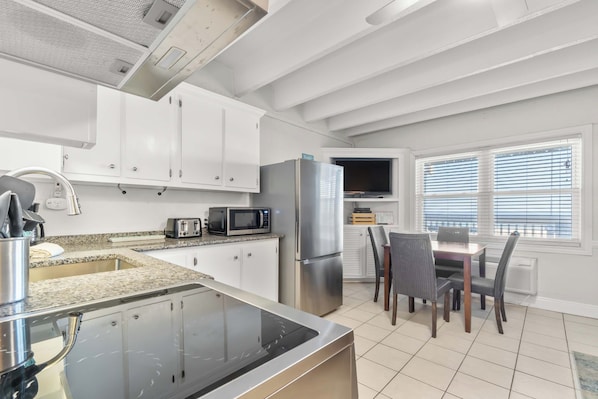 A modern kitchen with white cabinets, stainless steel appliances, a built-in microwave, and a dining area with a table and chairs. - Ocean-view condo with pool access, outdoor seating, central AC & WiFi (Gulf Shores)