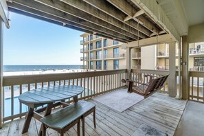 Une terrasse en bois avec une table et des chaises, donnant sur une plage et un immeuble doté de nombreux balcons.