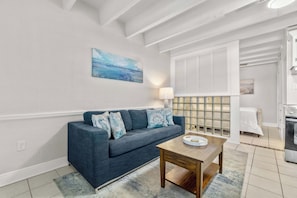 A modern living room with a dark blue sofa, a small wooden table, and a painting on the wall. - Ocean-view condo with pool access, outdoor seating, central AC & WiFi (Gulf Shores)