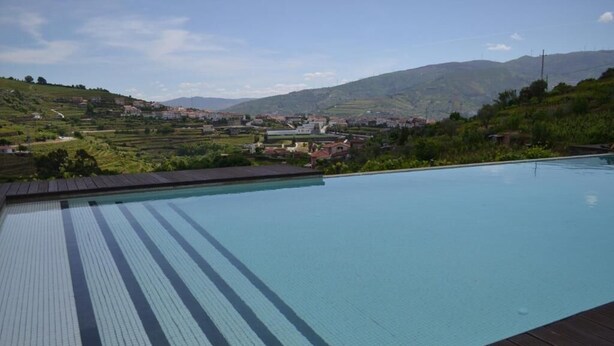 A swimming pool with a wooden deck and a view of a town and mountains in the background.