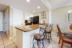 A kitchen with white cabinets, a black refrigerator, and a wooden island with bar stools. - Gulf-Front 6th-Floor Condo with Shared Outdoor Pool, CentralAC, Private Balcony (Gulf Shores)