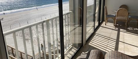 Un balcon avec vue sur la plage, des meubles en osier et un coin repas avec des chaises et une table.