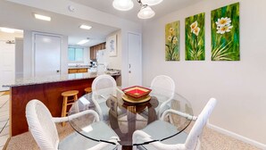 A dining area with a glass table, white chairs, a bar area, and three paintings on the wall. - 5th-floor beach-front condo with balcony, great views, & pool access (Gulf Shores)