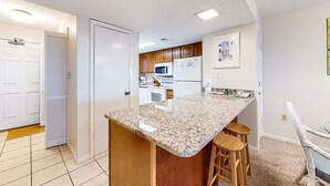 A kitchen with a granite countertop, wooden cabinets, and a refrigerator. - 5th-floor beach-front condo with balcony, great views, & pool access (Gulf Shores)