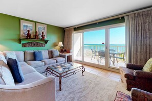 Ein Wohnzimmer mit Sofa, Sessel und einem Glastisch. Ein Balkon bietet Blick auf das Meer.