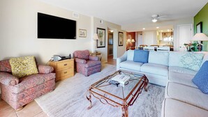 A living room with a sofa, armchair, coffee table, and a television. - Gulf-Front Condo with Shared Outdoor Pool, Private Balcony, Incredible Views & WiFi (Gulf Shores)