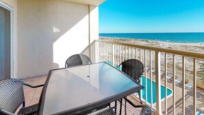 A balcony with a glass table and chairs, overlooking a beach and a swimming pool. - Gulf-Front Condo with Shared Outdoor Pool, Private Balcony, Incredible Views & WiFi (Gulf Shores)