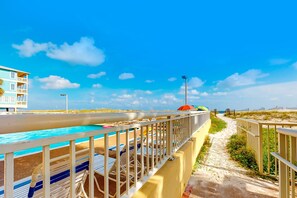 Un hôtel situé en bord de mer, doté d’une piscine, de chaises longues et d’un sentier menant à la plage.