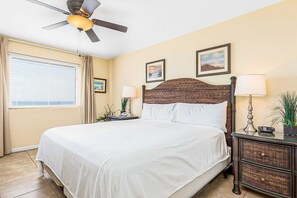 Une chambre à coucher comprenant un lit, un ventilateur de plafond, des tables de chevet et des œuvres d’art murales.