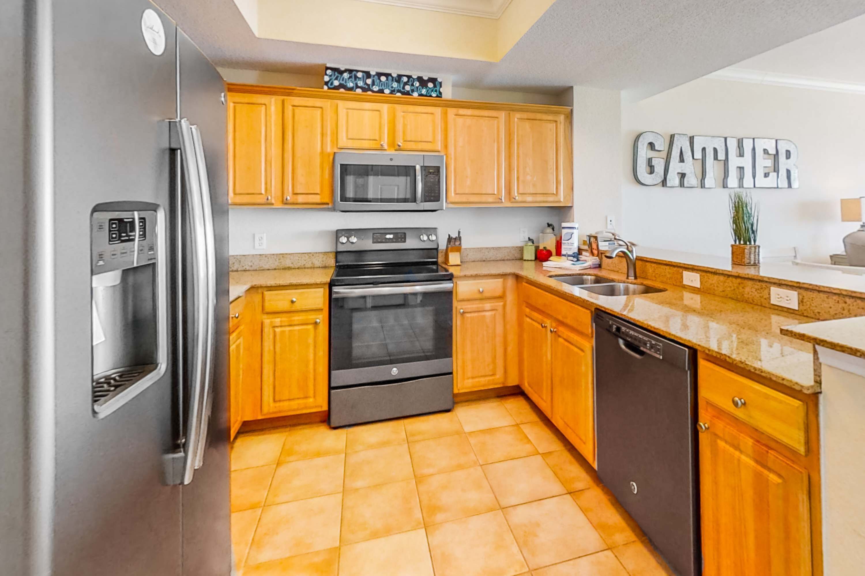 A modern kitchen with wooden cabinets, stainless steel appliances, and a 'GATHER' sign on the wall.