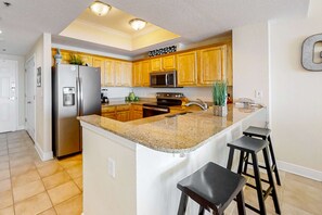 A kitchen with wooden cabinets, a stainless steel refrigerator, a microwave, a stove, and a granite countertop. - Beachfront 5th-floor condo with balcony, AC, pool, hot tub & view (Gulf Shores)