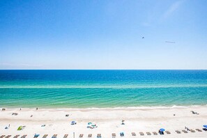 Ein Strand mit klarem, blauem Wasser, sandigem Ufer und einigen Sonnenschirmen und Liegestühlen.