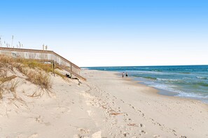 Een strand met een houten looppad dat naar het water leidt, zandstrand en voetsporen.
