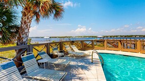 A pool area with lounge chairs, a palm tree, and a view of the water. - 2-Story Beach House w/Balcony, Washer/Dryer, Shared Pool, Snowbird-Friendly (Gulf Shores)