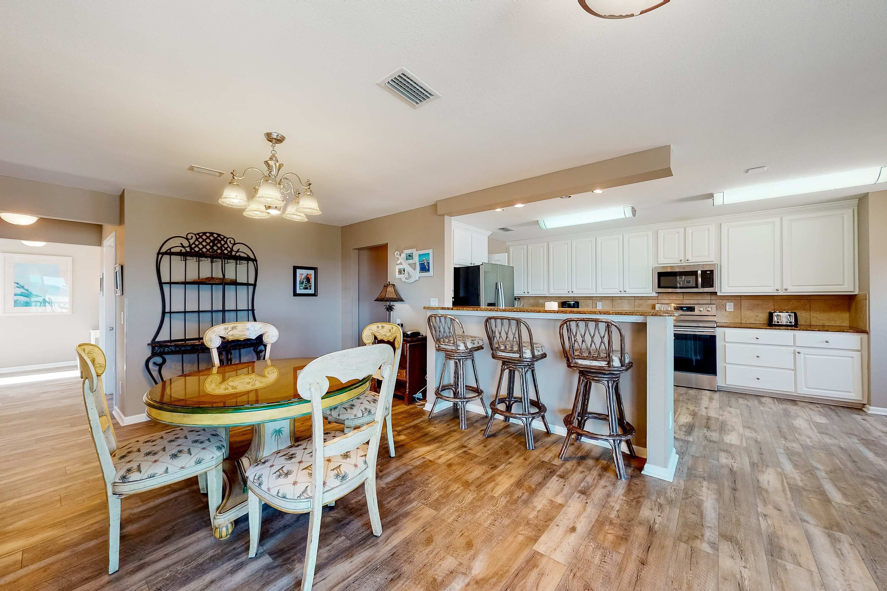 A spacious kitchen with white cabinets, a central island, and a dining area with a glass table and patterned chairs.