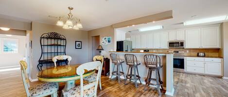 A spacious kitchen with white cabinets, a central island, and a dining area with a glass table and patterned chairs.