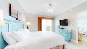 Um quarto com uma cama, ventilador de teto, televisão, cômoda e janela.