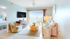 Sala de estar com televisão, sofá, mesa de centro e varanda com vista.
