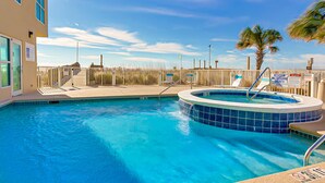 Piscina com ofurô, cerca de madeira e um edifício com grandes janelas.