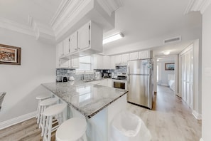 Eine moderne Küche mit weißen Schränken, einer Arbeitsplatte aus Granit, Edelstahlgeräten und einer Bar mit Hockern.