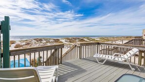 Eine Holzterrasse mit weißen Liegestühlen mit Blick auf Strand und Meer.