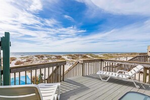 Eine Holzterrasse mit weißen Liegestühlen mit Blick auf Strand und Meer.