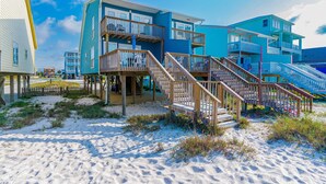Ein Strandhotel mit mehreren Balkonen, Holztreppen und einem Sandstrand.
