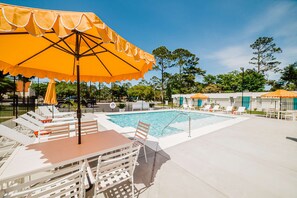 A swimming pool area with lounge chairs and umbrellas, surrounded by a fence and trees. - Comfortable single-level condo with WiFi, pool, & central AC (Gulf Shores)
