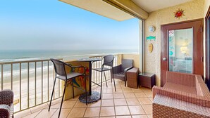 A balcony with a view of the beach, a table, chairs, and a wicker sofa. - Recently renovated 5th-floor oceanfront condo with pool, ocean view & WiFi (Gulf Shores)