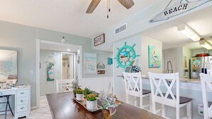A dining area with a wooden table, white chairs, and potted plants. - Recently renovated 5th-floor oceanfront condo with pool, ocean view & WiFi (Gulf Shores)