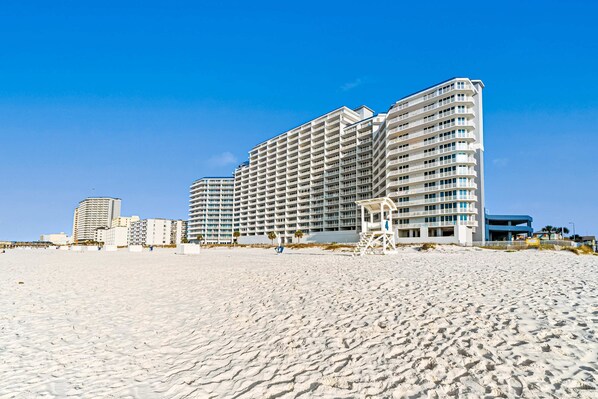 A beachfront hotel with multiple floors, a lifeguard tower, and a clear blue sky. - Gulf-Front Condo w Great Beach Views, Balcony & Shared Pools, Hot Tubs & Sauna (Gulf Shores)