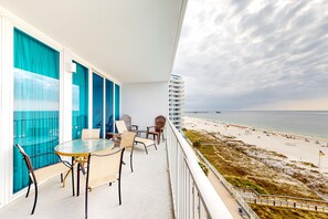 A balcony with a glass table and chairs, overlooking a beach and ocean. - Gulf-Front Condo w Great Beach Views, Balcony & Shared Pools, Hot Tubs & Sauna (Gulf Shores)