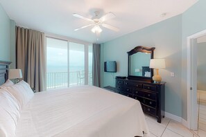 A hotel room with a large bed, a ceiling fan, a dresser, a television, and a balcony with a view. - Polished, Gulf-Front Condo w/ Balcony, AC, WiFi & Shared Pools/Hot Tubs/Sauna (Gulf Shores)