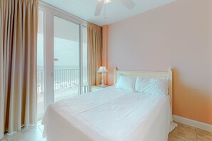 Ein Hotelzimmer mit einem großen Bett, einem Nachttisch, einer Lampe und Blick durch eine Schiebetür nach draußen.