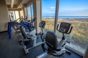 A gym with cardio machines and a view of the beach. - Gulf-Front Condo w Gorgeous Views, Balcony & Shared Pools, Hot Tubs & Gym (Gulf Shores)