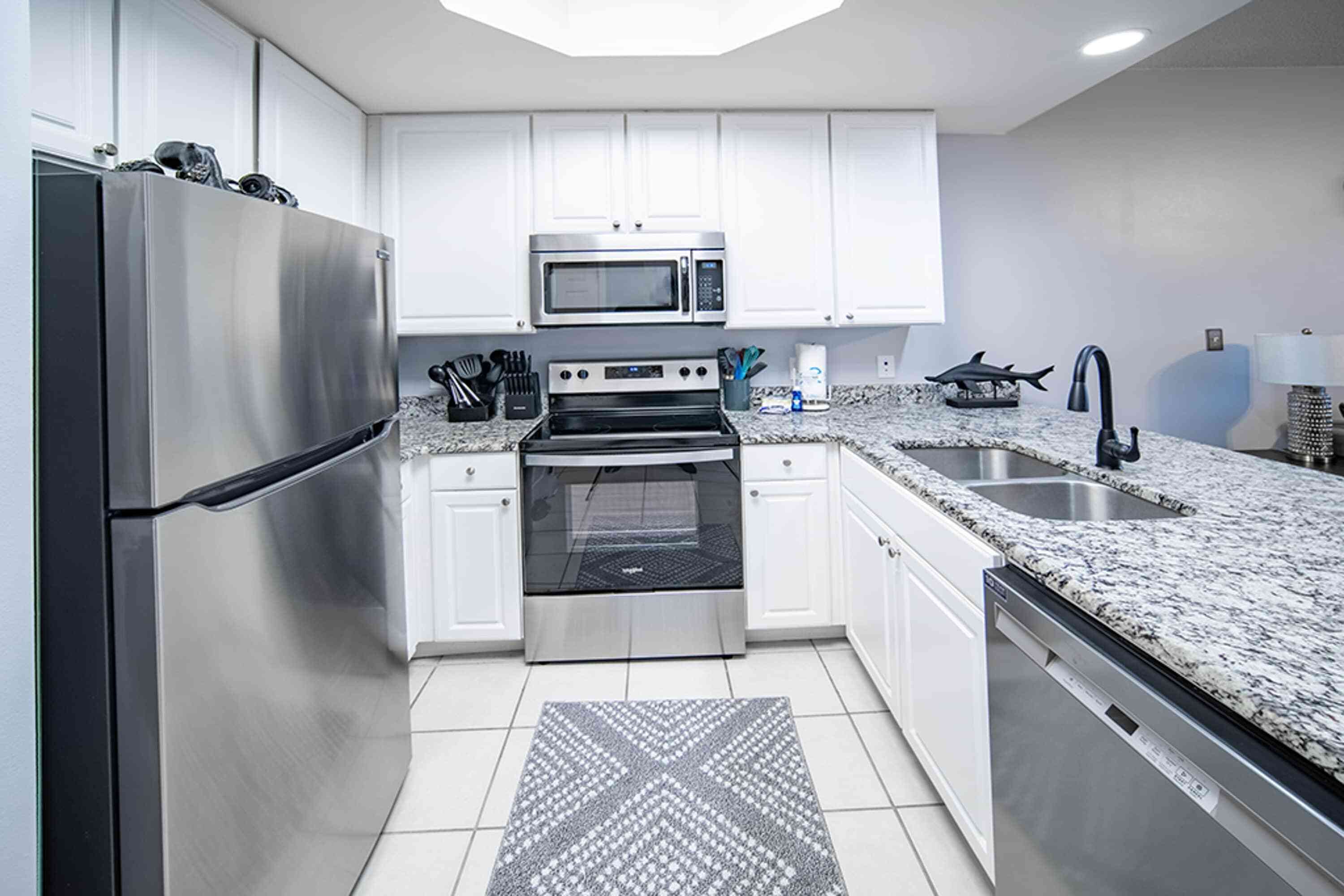 Una cocina moderna con electrodomésticos de acero inoxidable, armarios blancos, encimeras de granito y una alfombra estampada.
