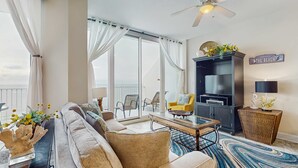 Ein geräumiger Wohnbereich mit einer Couch, einem Couchtisch, einer TV-Konsole und einem Balkon mit Sitzgelegenheiten.