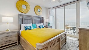 Ein Schlafzimmer mit einem Bett, einem Nachttisch, einer Lampe, einem Deckenventilator und einem Balkon mit Tisch und Stühlen.