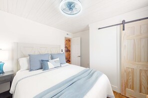 Un dormitorio con cama, mesita de noche, cómoda, puerta de madera y ventilador de techo.