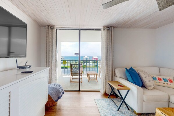 Una sala de estar moderna con un sofá, un televisor, una mesita y un balcón con vista al mar.