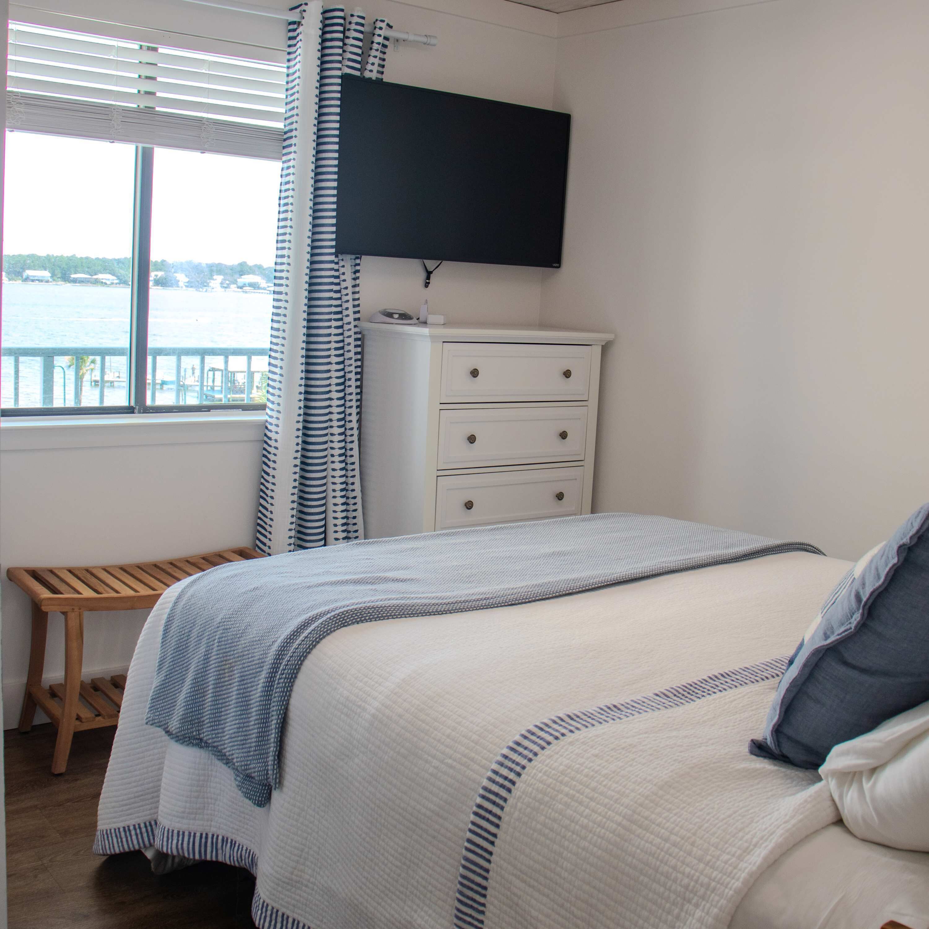 A bedroom with a bed, a dresser, a television, and a window with a view of the water.
