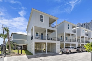 A multi-story residential building with balconies, a covered entrance, and a parking area with two trucks. - Inviting home with shared pool, balcony, full kitchen, central AC, & W&D (Gulf Shores)