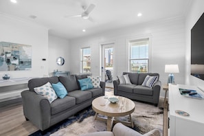 A modern living room with two grey sofas, a round coffee table, and a white cabinet. - Inviting home with shared pool, balcony, full kitchen, central AC, & W&D (Gulf Shores)