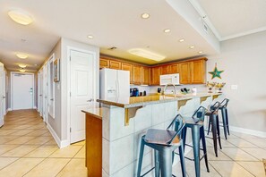 A kitchen with a central island, bar stools, wooden cabinets, and recessed ceiling lights. - Gulf-view retreat with washer,dryer, AC, pool, sauna, & fitness center (Gulf Shores)